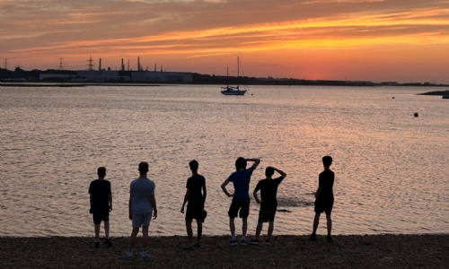 Students looking out over the water silhouetted against the sunset